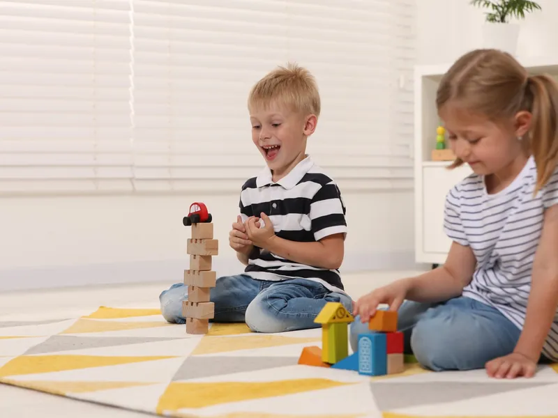 Zwei Kinder liegen auf einer Strickdecke und legen hölzerne Spielsteine eines Brettspiels vor sich aus.